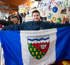 NWT speedskater Joshua Boudreau holds up the NWT flag in front of the Thunder Bay students whod rafted him, while holding support signs.