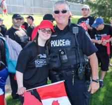 Mark Gugan, in his police uniform, poses for a photo with an athlete holding a Canadian flag.