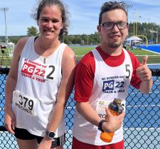 Two athletes smiling on the side of a track, one giving a thumbs up