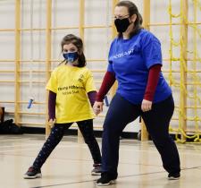 Active Start athlete and program leader holding hands while stretching their legs in a warmup