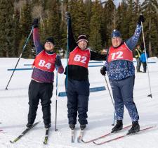 3 cross country skiers smiling holding their ski poles up