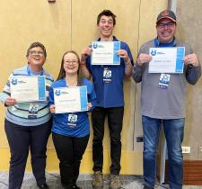 Four athletes smiling and holding certificates of achievement