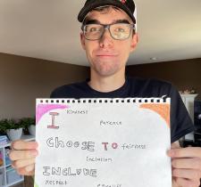 Josh holding a handwritten sign saying "I Choose to Include"