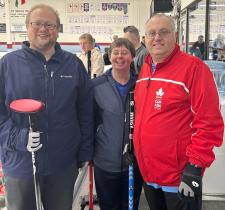 Three Special Olympics curling athletes smile at the side of the rink