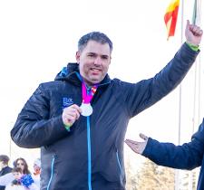 Ron raising one arm while holding his medal in the other