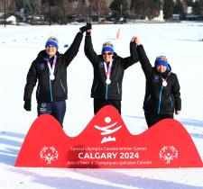 Three SO Team BC 2024 cross country skiing athletes on the podium, holding hands up together