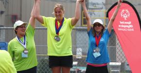 Kendall Salanski on top of podium raising hands with two other athletes