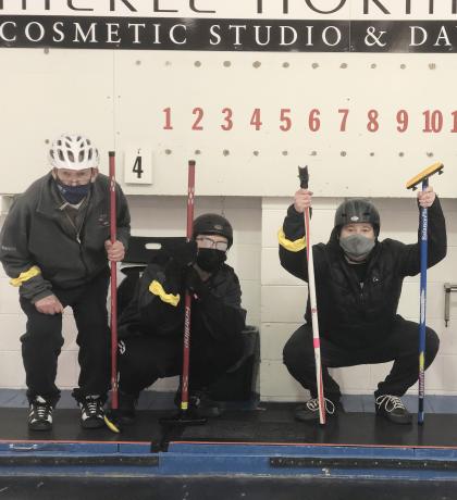 Curling athletes posing with their teammates and scoreboard