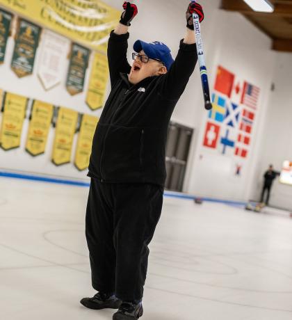 Curling athlete celebrates with both arms in the air