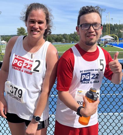 Two athletes smiling on the side of a track, one giving a thumbs up