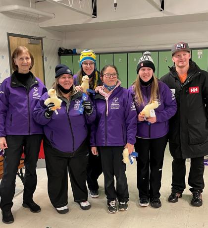 Debra Colvin standing and smiling with five of her athletes holding stuffed animal ducks and first place ribbons