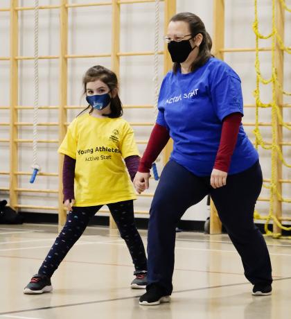 Active Start athlete and program leader holding hands while stretching their legs in a warmup