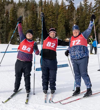 3 cross country skiers smiling holding their ski poles up