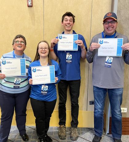 Four athletes smiling and holding certificates of achievement