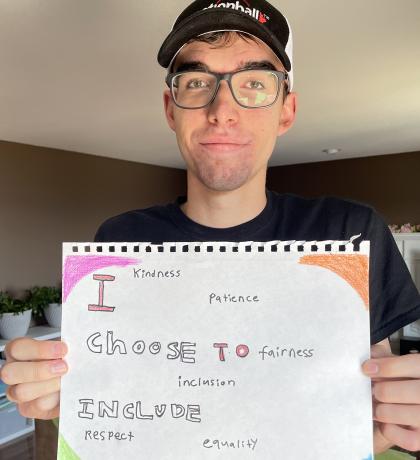 Josh holding a handwritten sign saying "I Choose to Include"