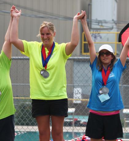 Kendall Salanski on top of podium raising hands with two other athletes