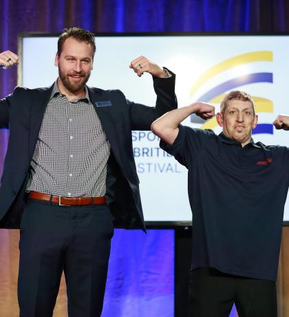 Canucks player Tucker Poolman and SOBC athlete Mike Palitti flexing their arms on stage