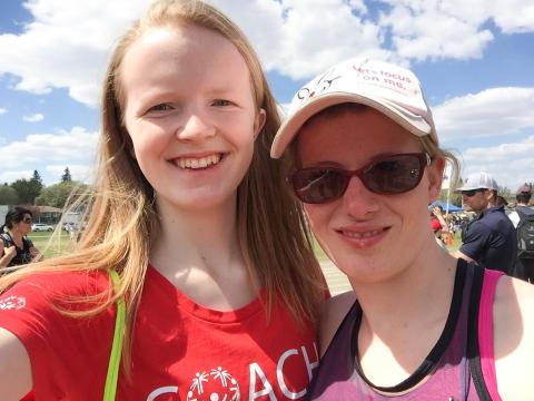 A young volunteer takes a selfie with an athlete outside on a sunny day