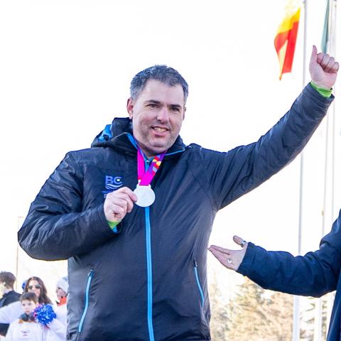 Ron lifting his arm up while holding his medal in the other