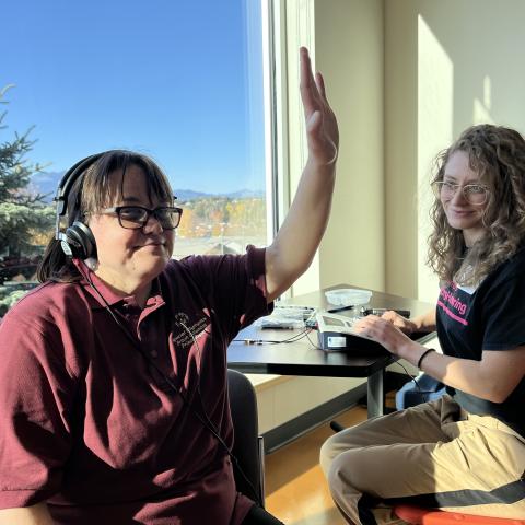 SOBC athlete with headphones on, smiling, and raising a hand up