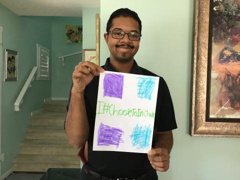 Special Olympics Calgary athlete and Tim Hortons employee Alex Arthur holds a I Choose To Include sign in his home