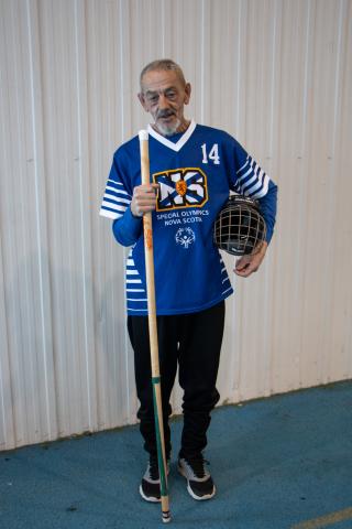 Richard Myette poses with his floor hockey stick and in his jersey, looking at the camera.