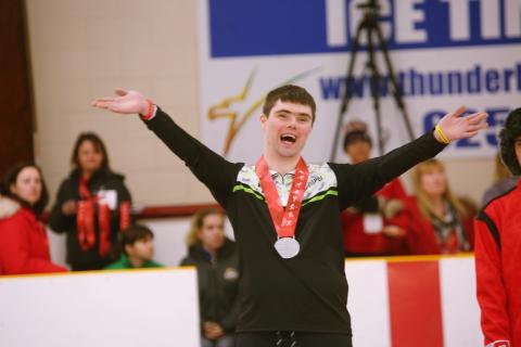 Jordan Koughan lifts his arms up in victory with a big smile on the podium