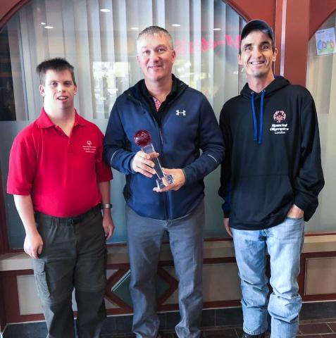 Mark McGugan poses for a photo holding an award with Special Olympics athletes next to him