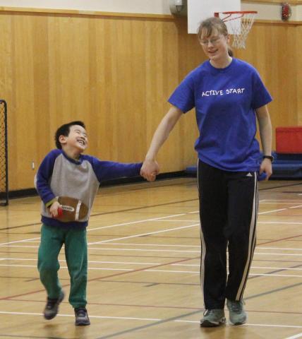 Active Start volunteer holding hands with child, both smiling