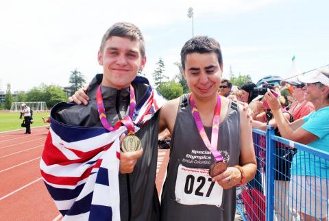 Two SOBC athletics athletes smiling with medals and BC flag around their necks