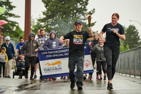 SOBC athlete holding torch and leading a group of Torch Run participants behind him holding LETR banner