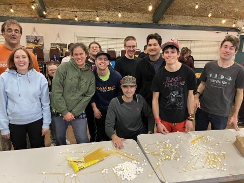 Group photo of snowshoeing athletes sitting at a table doing an activity with marshmellows and spaghetti sticks