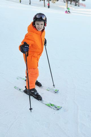 Wyatt poses for a photo on the ski hill in an orange snow suit