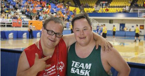 Two male athletes smile looking into the camera in front of a basketball court