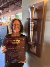 Sheri Lucas holding the plaque of the 2022 John Carion Award